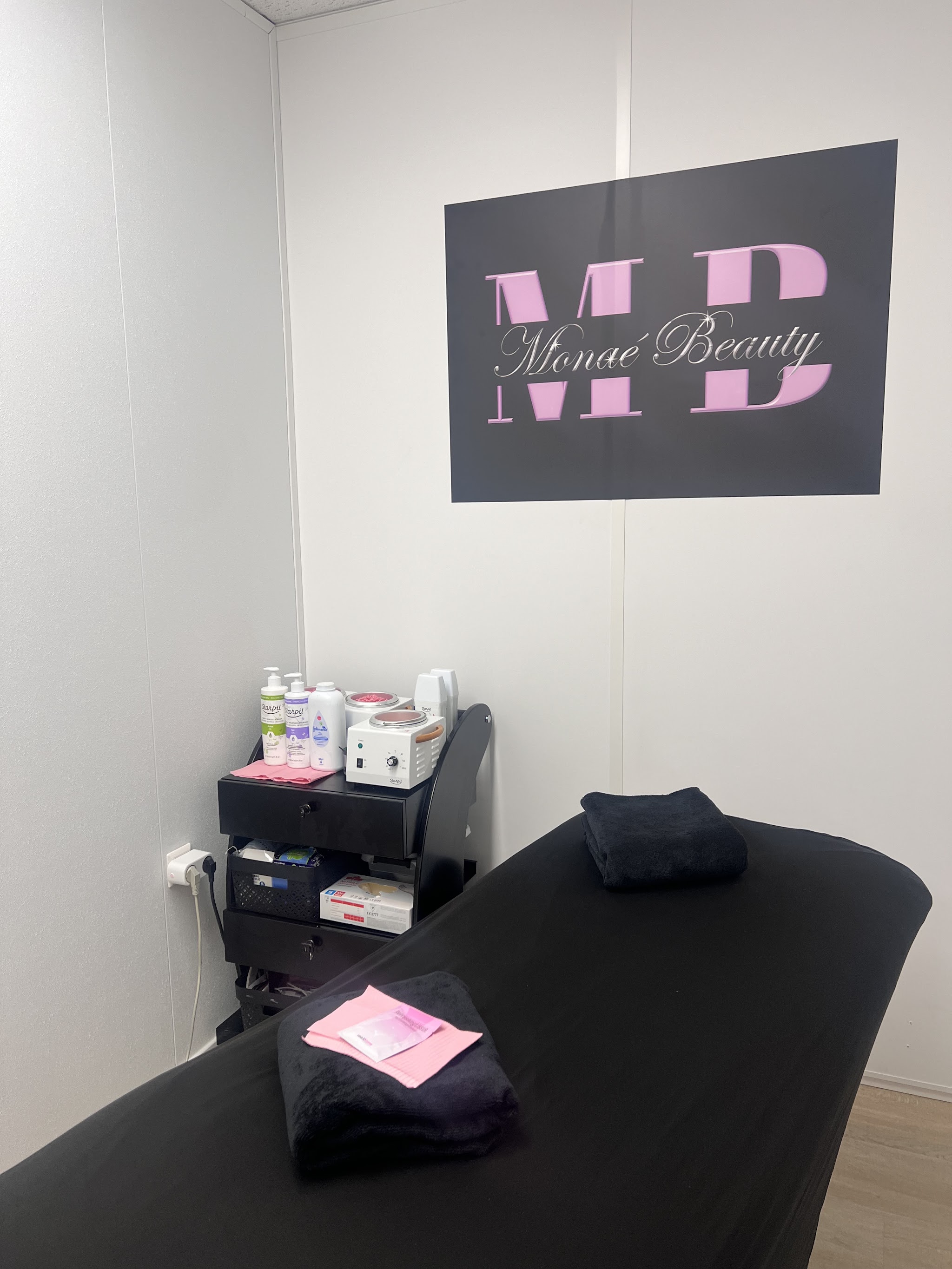 De behandelkamer van Monaé Beauty met een zwarte behandelbank en handdoeken